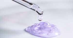 Tetesan serum asam eksfolian berwarna ungu dari pipet ke kaca