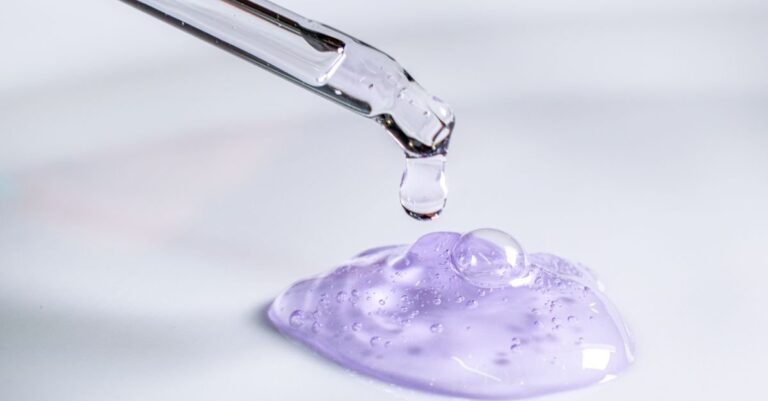 Tetesan serum asam eksfolian berwarna ungu dari pipet ke kaca