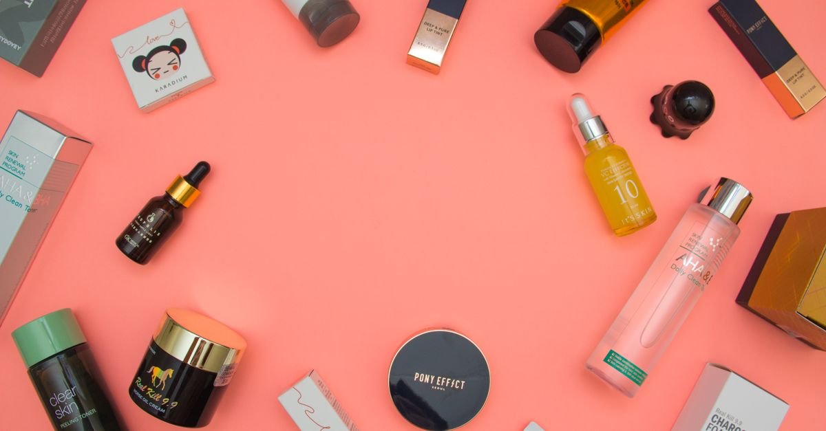 Berbagai botol produk skincare dan kecantikan tertata di atas latar koral, flat lay