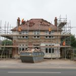 proyek renovasi rumah dua lantai aktif dengan scaffolding baja dan pekerja membongkar atap lama