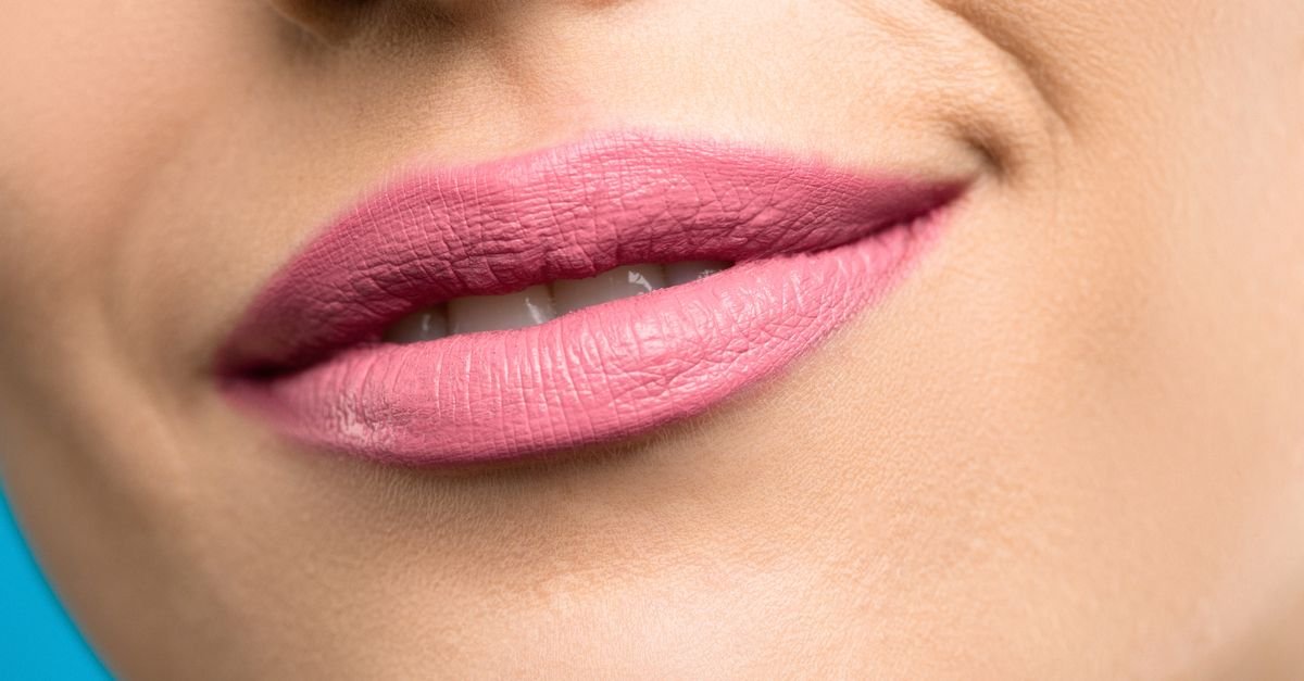 Close-up bibir pink dengan lipstick pada latar biru, detail filler bibir