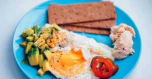 Piring sarapan sehat dengan telur alpukat roti dan tomat pada latar biru