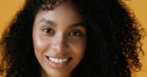 Wanita dengan kulit sehat dan natural di latar kuning hangat