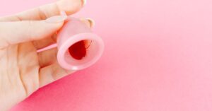 Tangan memegang cawan menstruasi pada latar pink, kesehatan wanita