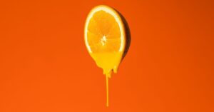 Tetesan kuning vitamin C pada latar oranye, konsep serum pencerah kulit