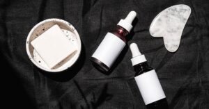 Botol serum pipet dan alat pijat wajah gua sha di latar gelap