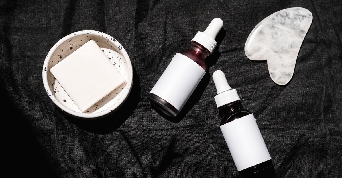 Botol serum pipet dan alat pijat wajah gua sha di latar gelap