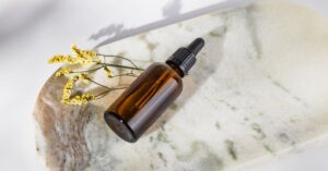 Botol dropper cokelat dengan bunga kuning kering di marmer