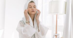 Wanita mengaplikasikan skincare di depan cermin pada malam hari, rutinitas malam